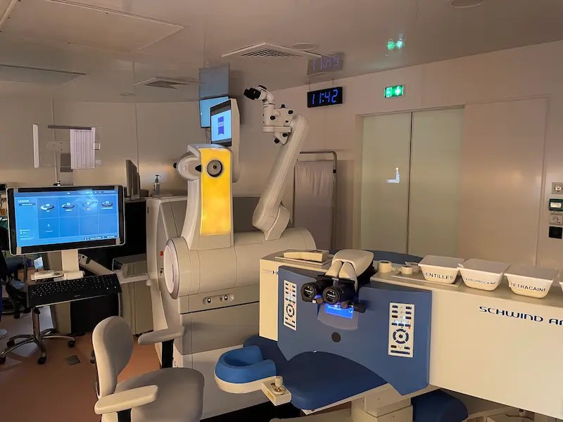 Salle de consultation ophtalmologique avec équipement moderne incluant des écrans, un microscope et des dispositifs de chirurgie réfractive.
